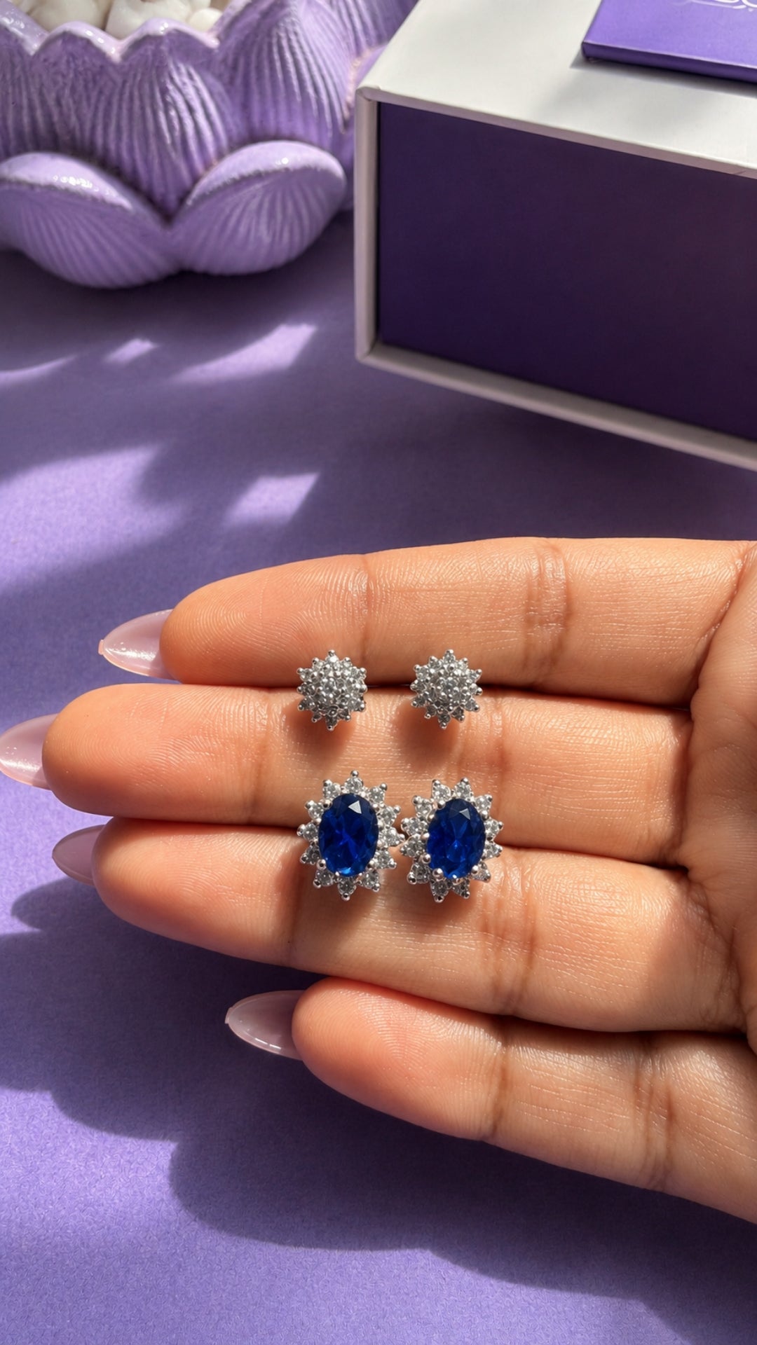 Midnight Duo in the hand beside the Nuqrah gift box: Lia zircon cluster tops and Lume synthetic sapphire tops in 925 sterling silver
